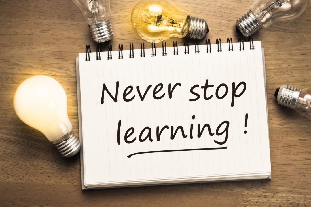 Never Stop Learning, handwriting quotation on notebook with light bulbs