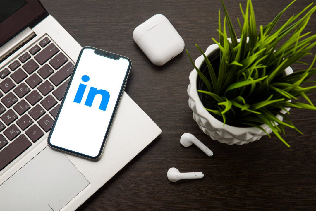 LinkedIn logo on the iphone X screen is placed on the laptop keyboard next to AirPods.