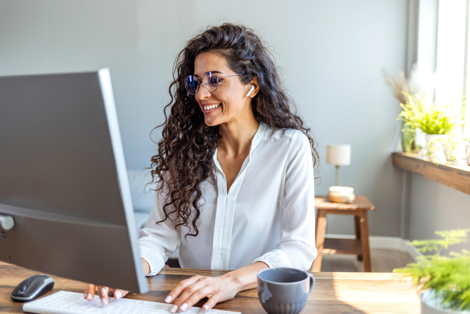 young business woman in white shirt and long curly hear smiling while working on her computer